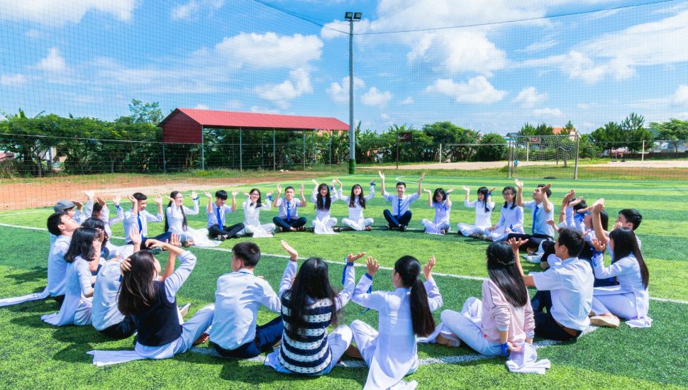 people sitting on green lawn grass while doing hands up at daytime