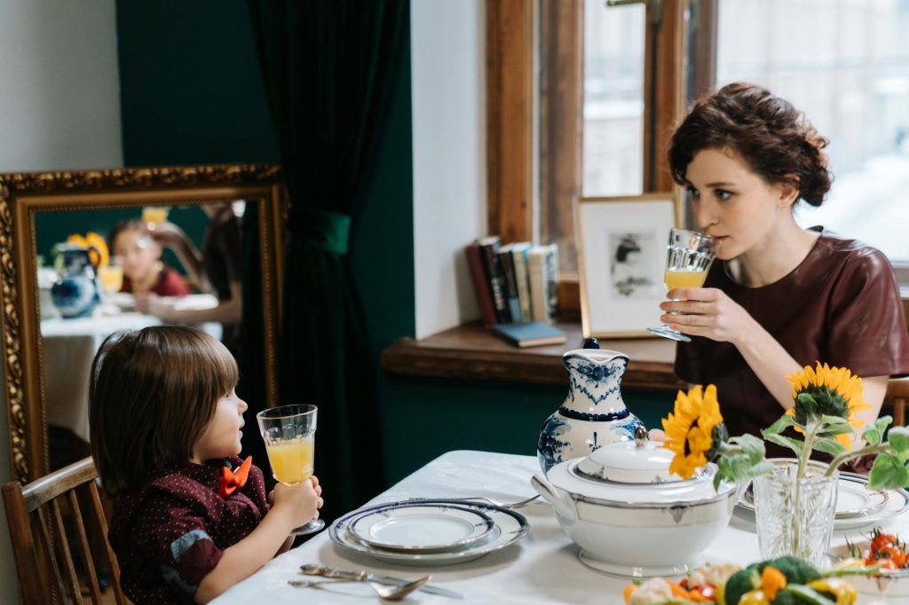 a babysitter teaching the kid how to properly drink a juice
