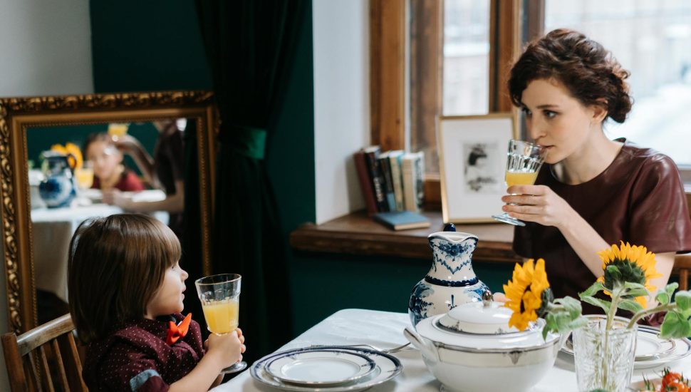 a babysitter teaching the kid how to properly drink a juice