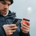 serious man paying online purchases using smartphone on street