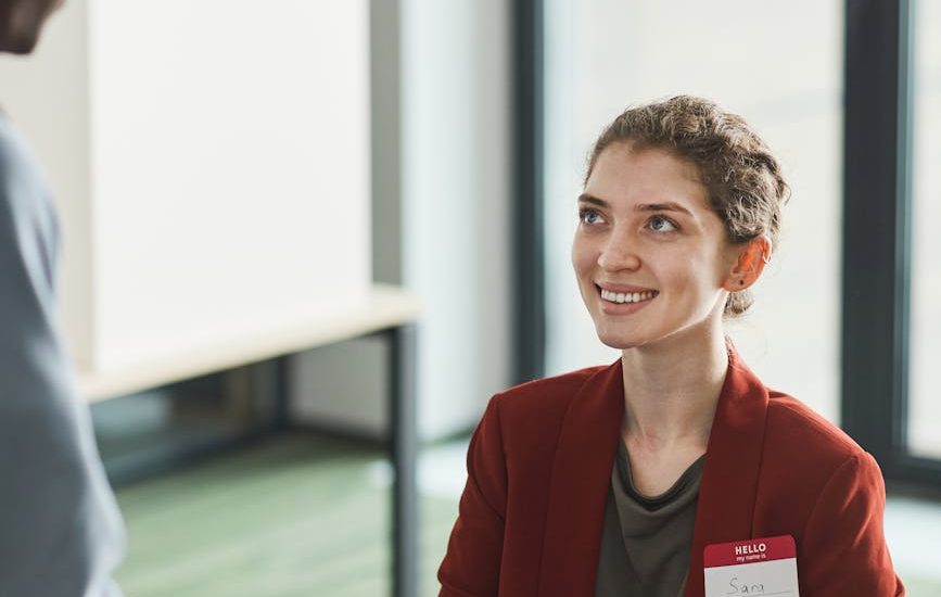 woman in orange blazer smiling handing a month a document